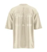 Remera de manga corta, corte relajado y color beige claro con efecto lavado. Presenta un estampado grande en la espalda en color blanco con el texto "Dropz Corp." sobre la silueta de un ángel en línea continua, junto a un código de barras y texto pequeño. En el frente lleva un logo sutil en el pecho.