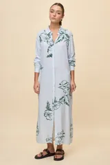 Vestido camisero largo de calce relajado, con patrón de rayas verticales celestes y blancas, y estampa floral en color verde. Posee cuello camisero, mangas largas y cierre frontal con botones.