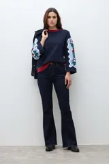 Sweater de punto color azul marino con diseño jacquard floral en las mangas y detalle de cuello redondo en color rojo. Presenta un corte holgado y mangas tres cuartos.