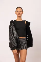 Campera reversible con capucha y cierre metálico frontal. Un lado está confeccionado en eco cuero negro con acabado brillante y el otro en corderito sintético negro. Cuenta con bolsillos laterales decorados con tachas piramidales plateadas, además de puños y cintura de rib elástico.