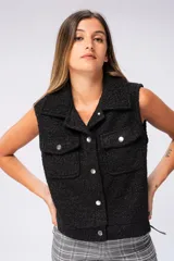 Chaleco negro de tejido boucle con cuello solapa, cierre frontal con botones metálicos, dos bolsillos de parche con botón en el pecho y corte recto.