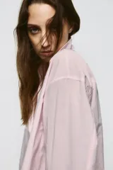 Camisa de corte oversize con cuello solapa y escote en pico. Presenta manga larga con puños abotonados, cierre frontal con botones y detalle de lazada ajustable en la espalda.