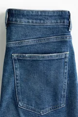 Jean tobillero de corte recto y tiro alto en denim de algodón con leve elasticidad. Presenta diseño de cinco bolsillos, cierre de botón y cremallera, y pliegues marcados al frente y en la espalda.