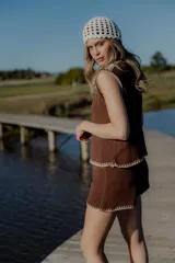 Conjunto de dos piezas tejido en algodón, compuesto por un chaleco sin mangas con cierre frontal de botones y un short de tiro medio. Ambas prendas presentan un diseño en color blanco con detalles de terminaciones en color beige.