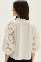 Blusa blanca de algodón con mangas abullonadas de broderie con diseño floreado. Presenta volados en el cuello y hombros, con un estilo romántico y femenino.