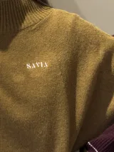 Buzo tejido de punto con cuello alto, diseño holgado y aberturas laterales. Presenta un cuerpo en color azul melange con detalles de franjas en color crema y verde en los puños y el ruedo. Incluye un pequeño bordado en el pecho.