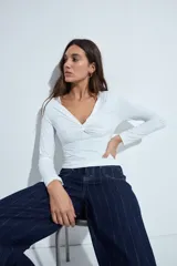 Top de manga larga blanco con escote en V y detalle de nudo fruncido en el centro del pecho.