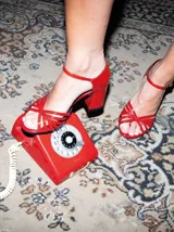 Sandalias de taco alto ancho con diseño retro, confeccionadas en charol negro. Presentan tiras delanteras múltiples entrelazadas, talón cerrado y una correa fina ajustable al tobillo con hebilla metálica.