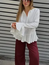Blusa blanca de textura arrugada, con escote en V y lazos para anudar. Presenta mangas largas con puños acampanados y un diseño con volado en el ruedo.