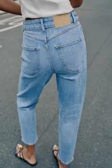 Jeans de tiro alto con diseño mom fit, tobilleros, de cinco bolsillos y cierre frontal con cremallera y botón, en color azul claro con efecto deslavado.