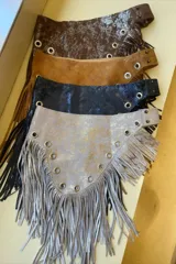Faja de cuero marrón con flecos largos y apliques metálicos en forma de tachas y estrellas.