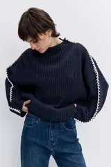 Jersey de punto color marrón chocolate, de cuello alto y corte holgado. Presenta un diseño acanalado y un detalle de costura decorativa en color blanco que recorre la parte superior de las mangas.