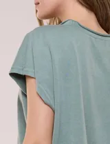 Remera de silueta amplia y relajada confeccionada en algodón y poliéster, de color verde, con escote a la base y mangas cortas de hombro caído. Presenta dobladillo enrollado y ruedo curvo.