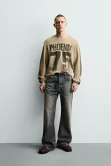 Sudadera de corte relajado confeccionada en tejido con textura waffle, color beige con efecto lavado. Presenta cuello redondo, manga larga con franjas laterales oscuras y estampado frontal con texto y número en contraste.