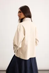 Sobrecamisa de algodón color beige, de corte holgado, con bolsillos frontales aplicados, cuello camisero y puños en contraste con estampado de cuadros en tonos verde oscuro. Cuenta con cierre frontal de botones metálicos.