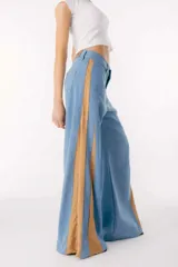 Pantalón de jean azul de pierna ancha, con tiras laterales en tono tostado y apliques geométricos con textura.