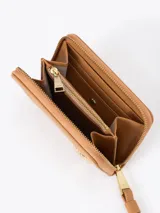 Billetera compacta de cuero vacuno color bordó, con cierre perimetral, correa de muñeca y aplique metálico dorado en forma de mariquita en el frente.