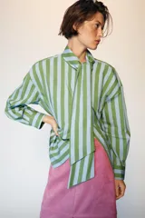 Camisa de rayas rojas y celestes, con cuello subido y lazada en el mismo tejido, manga larga con puños y bajo asimétrico.