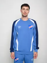 Buzo de entrenamiento o casual del Club Nacional de Football, color celeste/azul claro con mangas azul marino y detalles en blanco en los hombros y costados. Presenta el logo Umbro y el escudo del C.N.d.F. bordados.