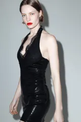 Vestido corto de lentejuelas negras con cuello halter y escote en pico profundo. Presenta detalles de encaje en el escote y espalda descubierta con cierre de botones en el cuello.