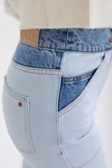 Pantalón de jean celeste con cintura alta y corte recto. Presenta un diseño color block con secciones en denim de tono más oscuro en la cintura y en la parte inferior de las piernas.