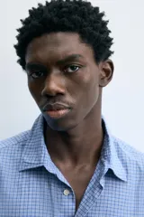 Camisa de hombre de manga larga, color azul, con cuello solapa y bolsillo plastrón en el pecho. Presenta un patrón de cuadros pequeños en tonos de azul y blanco.