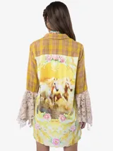 Camisa de algodón a cuadros en tonos amarillos y marrones, con mangas largas que terminan en volantes de encaje beige. Presenta botones metálicos frontales, uno de ellos con detalle de cristal, y un aplique floral bordado en 3D en una de las mangas.