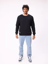 Buzo de cuello redondo color negro, con puños y ruedo acanalados. Presenta una pequeña etiqueta decorativa en el lateral inferior derecho.