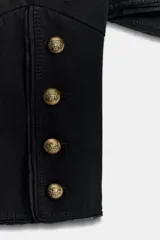 Chaqueta de estilo militar en color negro, con cuello redondo y cierre frontal mediante alamares decorativos. Presenta mangas largas con botones en los puños y forro interior a tono.