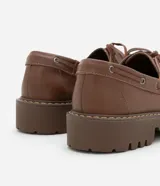 Zapato estilo dockside de cuero color marrón, con puntera redonda, cordones frontales y suela track dentada.
