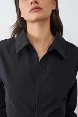Camisa de popelina negra de manga larga, con cuello clásico y cierre frontal de cremallera con abertura en el bajo.