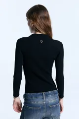 Chomba de punto acanalado color negro, con cuello polo, escote en V con botones y mangas 3/4 con puños de lurex. Presenta un diseño ajustado al cuerpo y un detalle metálico en la espalda.