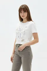 Remera de algodón blanca, de corte holgado, con cuello redondo y mangas cortas. Presenta un estampado frontal con motivos marinos que incluye una ballena, caballitos de mar y caracoles.