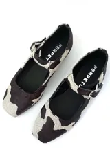 Zapato Mary Jane con estampado de vaca en blanco y negro, con correa al tobillo y hebilla plateada.