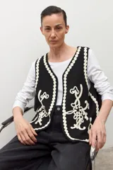 Chaleco tejido negro con escote en V, sin mangas y bordados en color crema con motivos florales y detalles de ondas en los bordes.