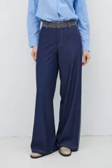 Pantalon de corte recto y tiro alto, confeccionado en denim azul oscuro con costuras a contratono. Presenta una cintura con detalle de estampado a cuadros y una franja lateral clara que recorre toda la pierna.