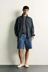 Camisa relaxed fit de lino color negro con efecto lavado, cuello clásico, manga larga con puños abotonados y dos bolsillos de parche con solapa en el pecho.