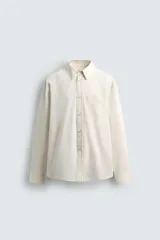 Camisa de corte relajado confeccionada en tejido fluido con textura jacquard de rayas verticales. Presenta cuello clásico, cierre frontal con botones, manga larga con puños abotonados y un bolsillo de parche en el pecho.
