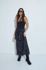 Falda larga de corte fluido con estampado animal print en tonos oscuros. Presenta un detalle de lazo anudado en la cintura y terminaciones con borde ondulado.