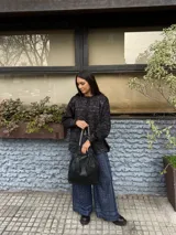 Cartera tipo hobo de cuero negro con diseño fruncido en la parte superior y asa de cadena metálica plateada.