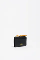 Monedero pequeño de estructura rígida, color negro, con cierre de cremallera y tirador de tejido amarillo mostaza. Presenta un bolsillo exterior frontal y el logo de la marca grabado en dorado.