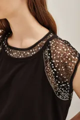 Remera de jersey de algodón grueso color crema, con mangas cortas y cuello redondo. Las mangas y el cuello son de microtul bordado con lentejuelas doradas.