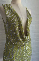 Vestido corto ajustado color verde lima, con escote pronunciado en V tipo drapeado y tirantes finos. El vestido está cubierto de lentejuelas plateadas.