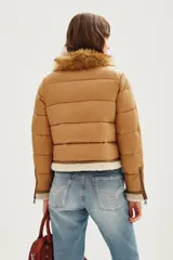 Campera estilo aviador en tonos tostados, con diseño acolchado y paneles de gamuza en la parte superior. Presenta cuello alto con doble hebilla, cierre frontal completo y detalles de corderito sintético en el cuello y el ruedo.