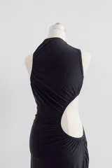 Vestido midi negro con diseño drapeado, cuello alto, abertura lateral en la cintura (cut-out) y un solo hombro descubierto.