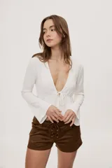 Blusa blanca de manga larga con escote profundo en V, ajuste regulable con lazo delantero y diseño fluido con vuelo en las mangas y la cintura.