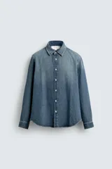 Camisa de corte relajado confeccionada en denim de algodón con efecto lavado. Presenta cuello solapa, cierre frontal de botones y mangas largas con puños abotonados.