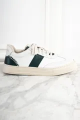 Zapatillas urbanas de cuero blanco con una franja lateral verde oscuro y suela color crema.