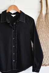Camisa negra de manga larga con cuello clásico, cierre frontal con botones y volados verticales en el frente.