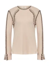 Remera de manga larga color beige, confeccionada en tejido de punto tipo waffle. Presenta detalles artesanales de crochet en tono marrón oscuro a lo largo de las mangas, hombros y puños, con cuello redondo.